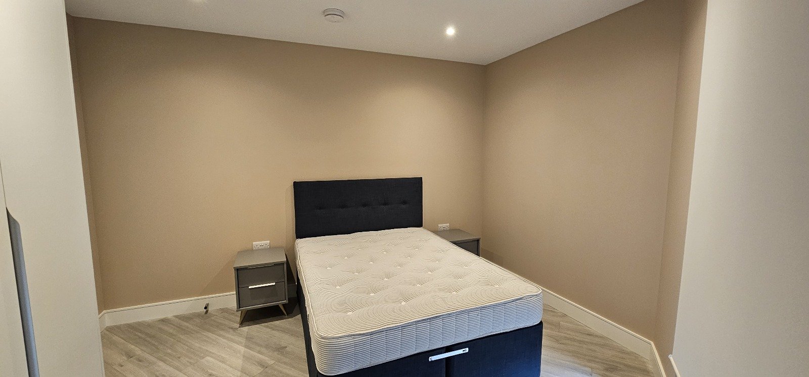Bedroom with beige walls, a bed with a black headboard and grey bedside tables.