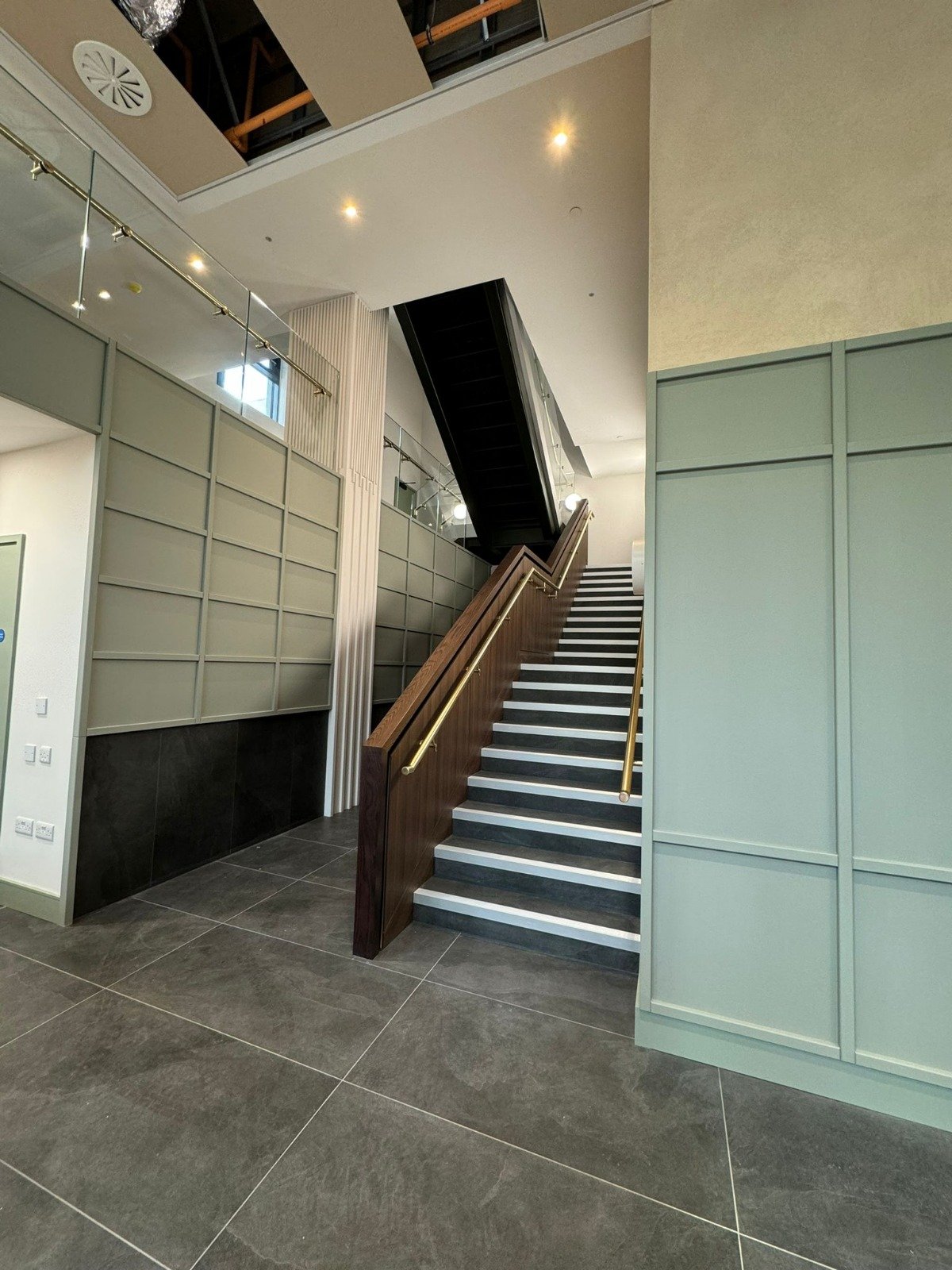 Interior staircase with wooden handrails, black steps and light green paneling.